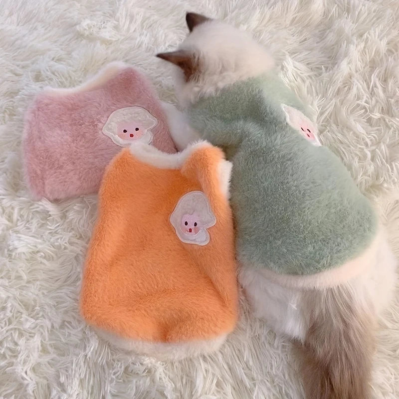 Three soft fleece cat vests for winter in orange, green, and pink with cute animal designs