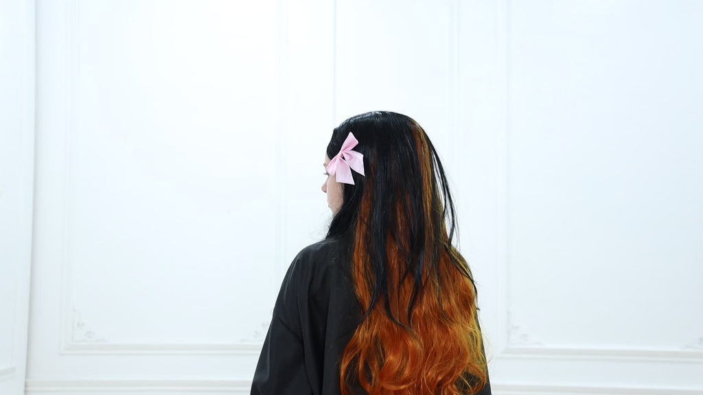 Model wearing anime kimono cosplay costume with long black and orange hair and a pink bow