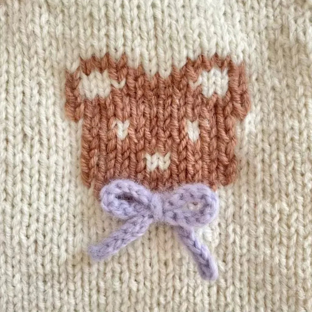 Close-up of a beige knit dog sweater with bear design featuring a bear face and bow detail
