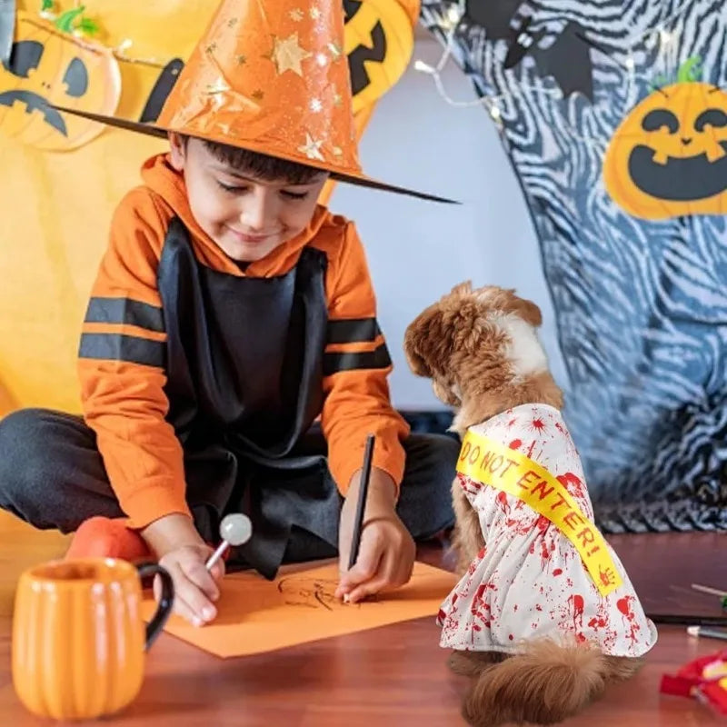 Small dog wearing a blood splatter dog dress, sitting beside a child in a Halloween setting