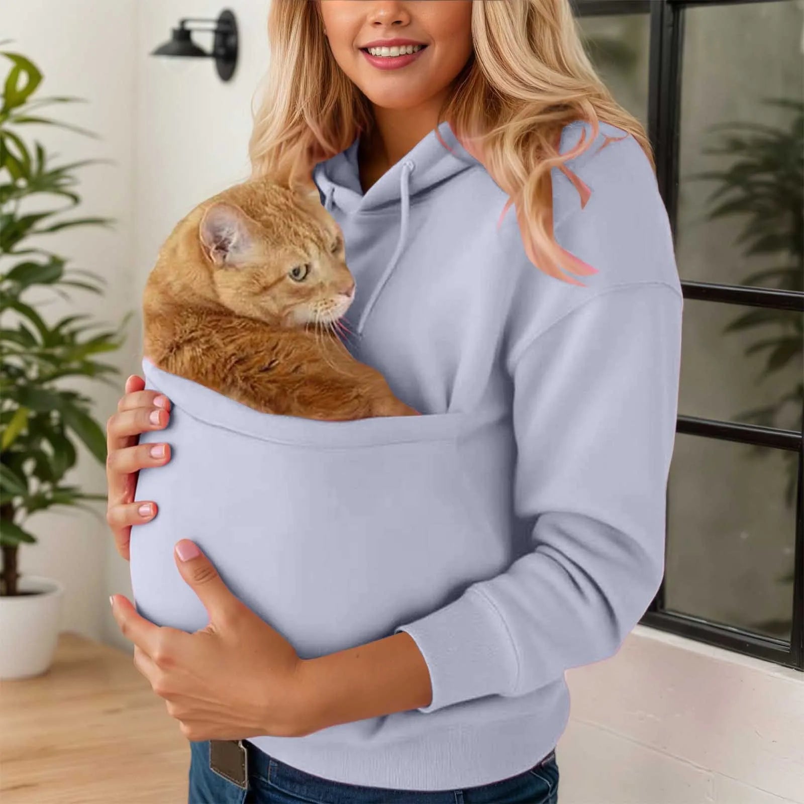 Woman wearing a cat carrier kangaroo pocket sweatshirt with an orange cat nestled inside