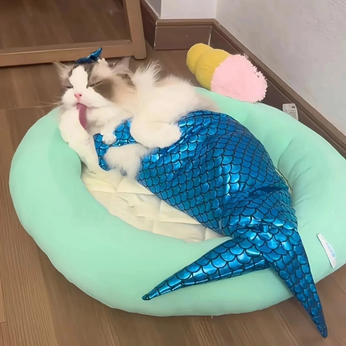 Fluffy cat wearing a cat mermaid costume lying comfortably on a pet bed