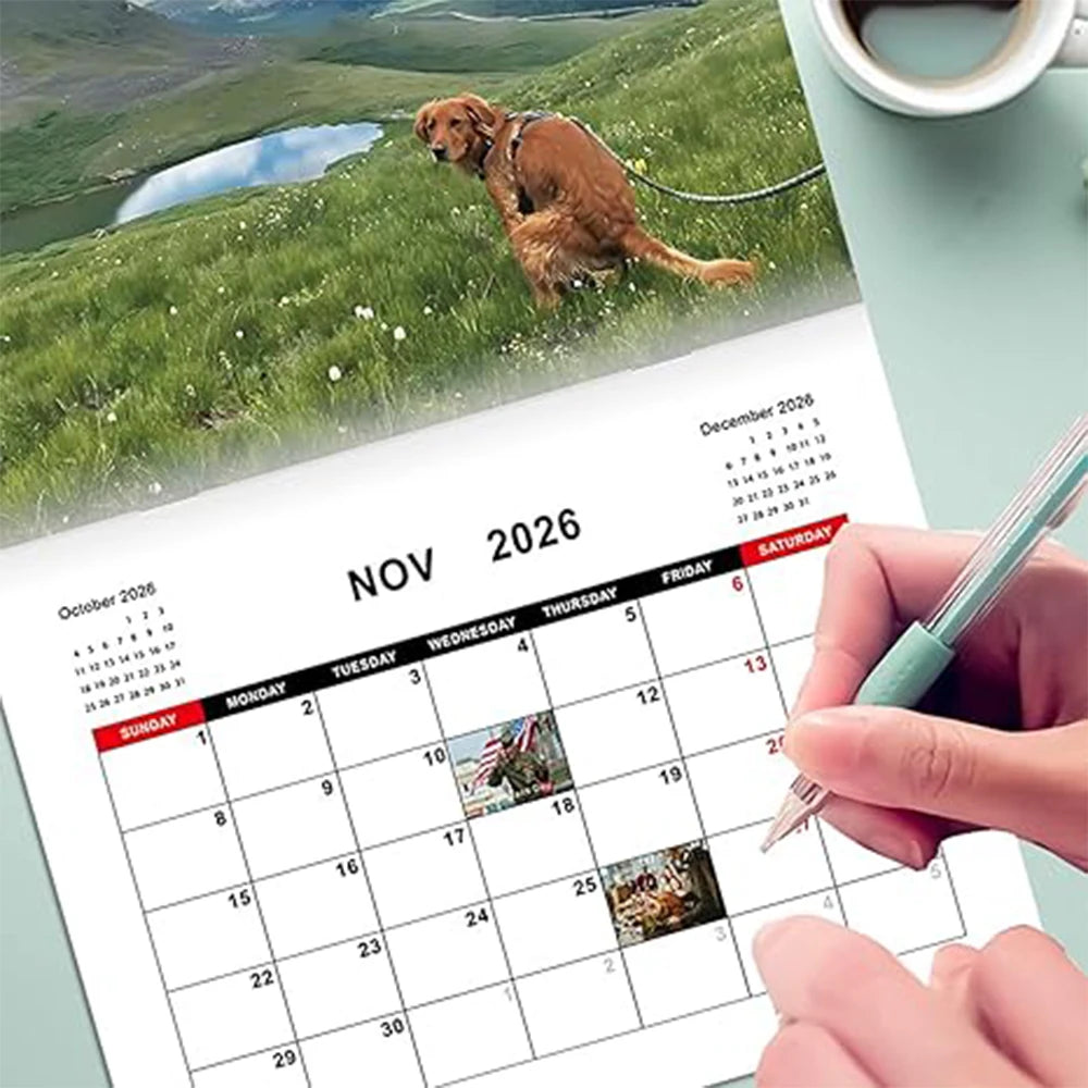Dogs pooping in scenic places calendar displayed on a desk with a hand holding a pen
