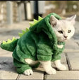 Cute white cat wearing a green pet dinosaur costume for cats and small dogs with spikes on the back